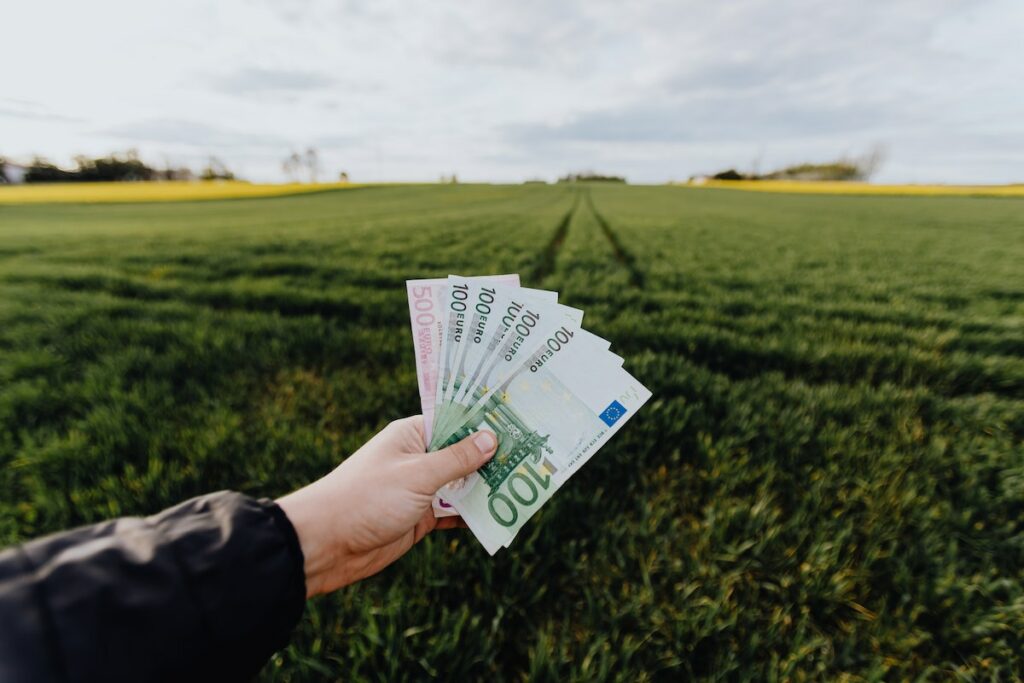 Crop-farmer-showing-money-in-green-summer-field-in-countryside